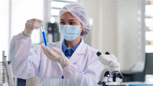 Asian adult woman scientist researcher holding test tube blue liquid performing experiment analysis laboratory professional focused work healthcare innovation medical development scientific study