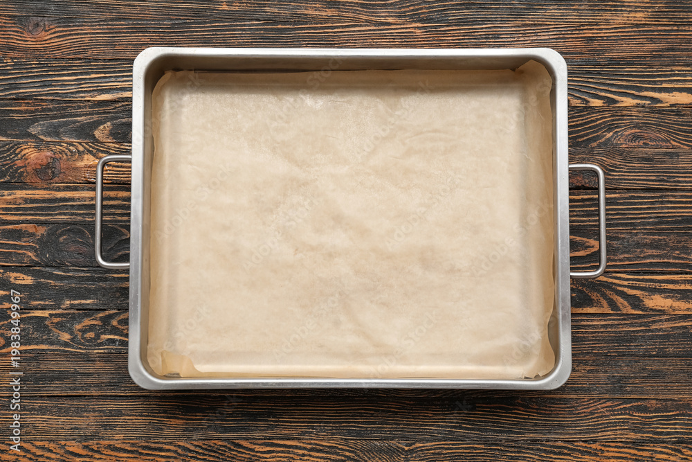 Obraz premium Metal baking tray with parchment paper on wooden background