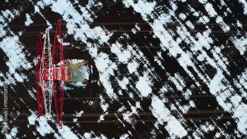 Drone shot of power transmission towers and cables standing in snowy winter countryside.