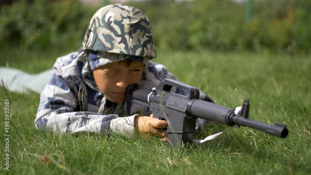 Fototapeta premium boy in camoflauge playing war shoots a toy gun, have fun and enjoy