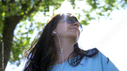 Fotografie Young woman relaxing outdoors listening to music and smiling, have fun and enjoy