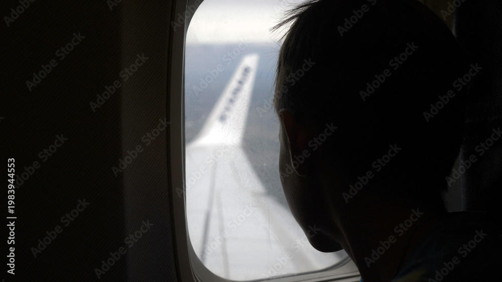 Fototapeta premium boy looks out the porthole during landing airplane, have fun and enjoy