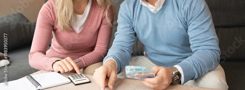Canvas Print Mature couple managing finances at home, using a calculator and counting euros