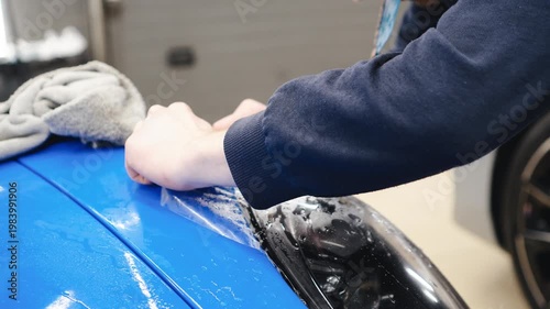 Detailer worker smoothes PPF, Paint Protection Film on blue sport car Headlight. The process of installing PPF film on the headlight of the blue car. A car wrapping specialist applies a PPF. 