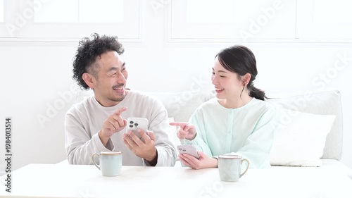 リビングでスマホを見て笑顔の日本人夫婦