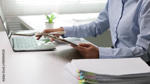 Asian businesswoman reviewing financial documents and using a calculator at her desk. Professional accountant working on a report.
