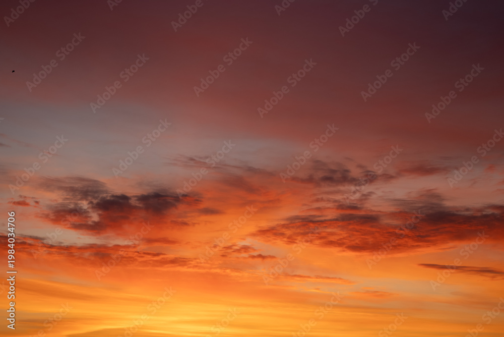 Fototapeta premium Evening sky displaying a beautiful blend of fiery colors from orange and red to soft yellow and purple, with delicate cloud formations enhancing the tranquil and dramatic ambiance of dusk