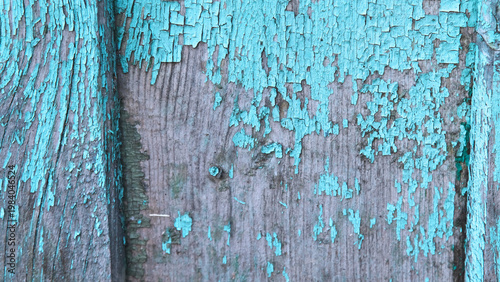 Old wooden board texture with heavily peeling and cracked turquoise paint close-up.