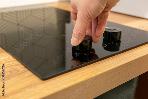 Person turns on a black kitchen stove with a wooden countertop while preparing a meal in the kitchen