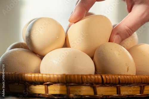 Many eggs in a basket with a hand reaching for one during morning light in a kitchen
