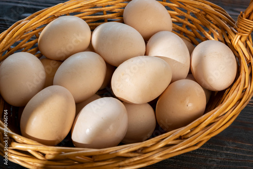 Fresh eggs placed in a brown woven basket on a wooden surface in a kitchen setting during the day