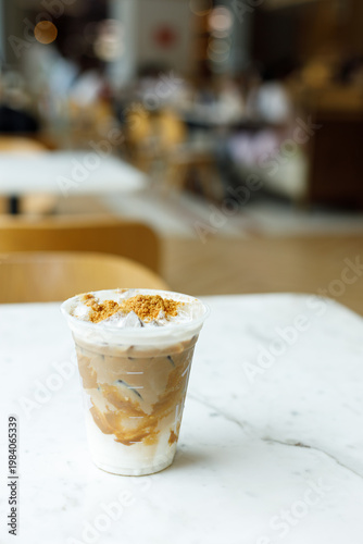 Cup of iced milk caramel latte coffee topped with biscuit on table by the window.