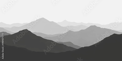 A misty mountain landscape at sunrise reveals a vast range of peaks and valleys under a blue morning sky where clouds and fog drift over the silhouetted hills and horizon