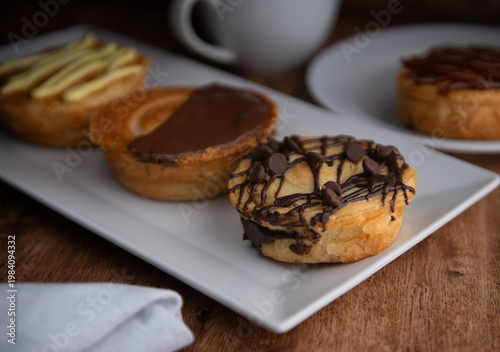 Reposteria casera, pan de hojaldre sobre un plato blanco para disfrutar en familia con cafe o leche, chispas de chocolate encima y servilleta de tela al lado