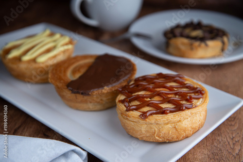 Reposteria casera, pan de hojaldre sobre un plato blanco para disfrutar en familia con cafe o leche, vainilla cajeta y chocolate con taza de cafe al fondo