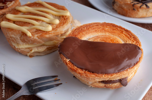 Reposteria casera, pan de hojaldre sobre un plato blanco para disfrutar en familia con cafe o leche, con chocolate oscuro encima y un tenedor al lado.