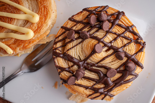 Reposteria casera, pan de hojaldre sobre un plato blanco para disfrutar en familia con cafe o leche, con chispas de chocolate y un tenedor al lado.