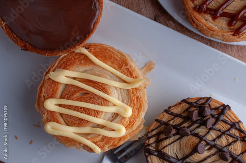 Reposteria casera, pan de hojaldre sobre un plato blanco para disfrutar en familia con cafe o leche, cubierta de ctrema pastelera de vainilla, vista cenital.