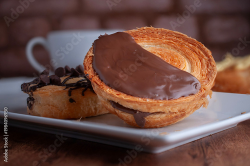 Reposteria casera, pan de hojaldre sobre un plato blanco para disfrutar en familia con cafe o leche, cubierta de chocolate oscuro