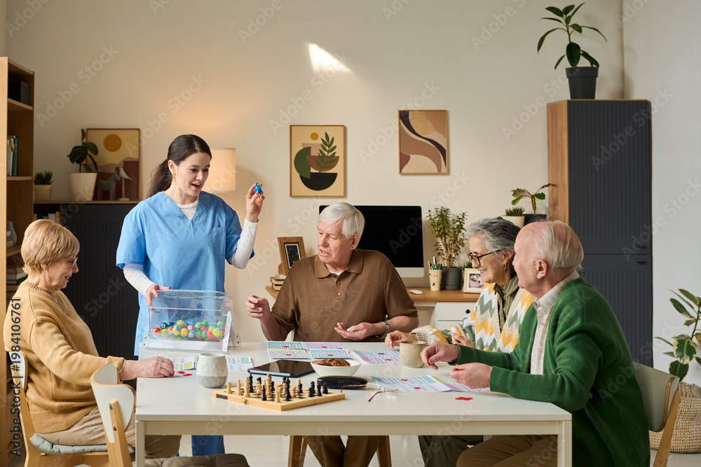 Obraz premium Senior group playing game with female caregiver in care home, engaging in cognitive activity and social interaction. Useful for eldercare, assisted living, dementia support marketing
