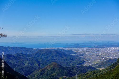 Expansive mountain and coastal view on Shikoku Henro overlooking city and sea under clear blue sky in Japan