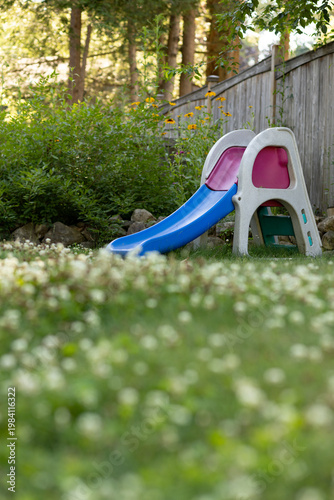 Child's slide in a backyard surrounded by green grass and flowers