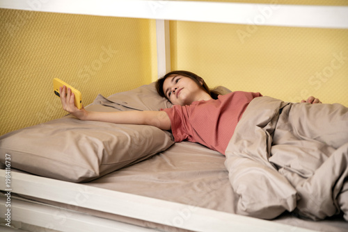 girl lies in bed; she has been woken up by her smartphone.