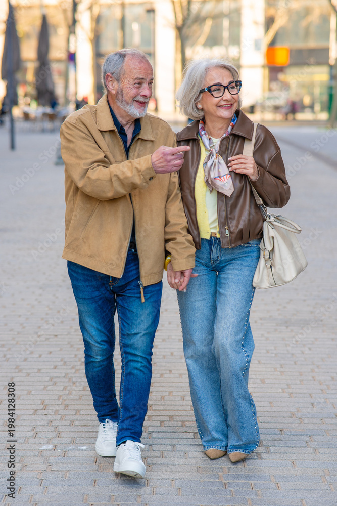 Fototapeta premium Smiling senior couple holding hands walking city street