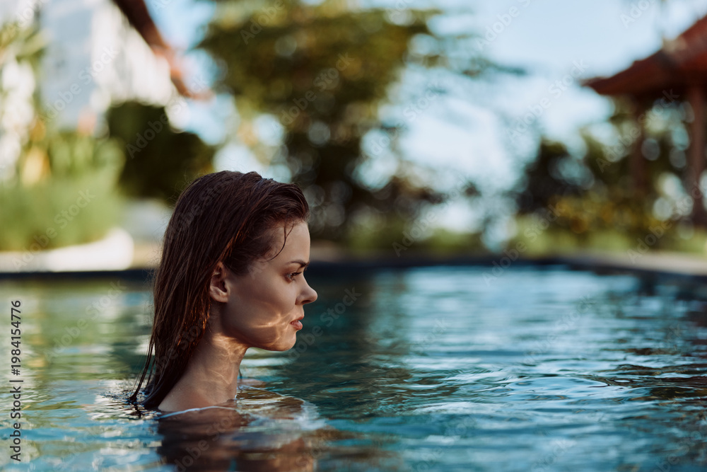 Fototapeta premium Serene woman with wet hair in a pool, side profile, enjoying a sunny day. Water reflections glow on blue surface, outdoor setting, casual wellness and leisure. Calm mood, fresh air, self care through