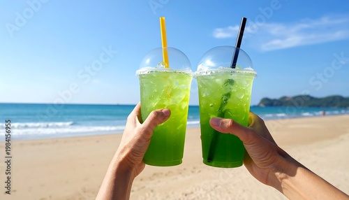 Two hands holding green drinks on a sunny beach, celebrating