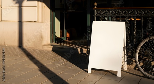 Blank white sandwich board sign stands outside a shop, ready for advertising messages.