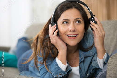 Fotografie woman on sofa lifting headphone from her ear
