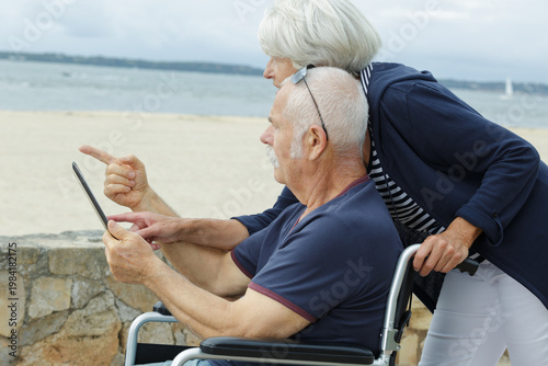 senior couple by the beach with tablet man in wheelchair