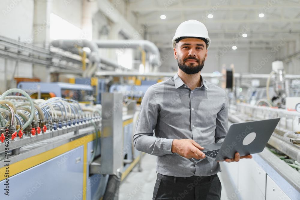 © Serhii - Industrial engineer holding laptop, managing production line in factory