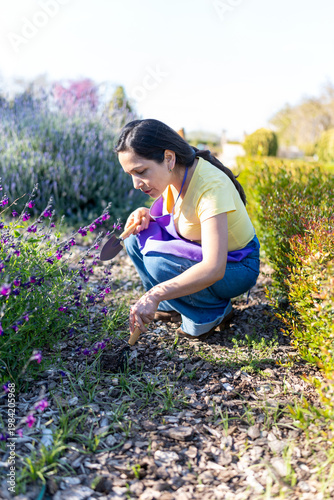 Latin woman gardening and cultivating flowers using gardening tools outdoors
