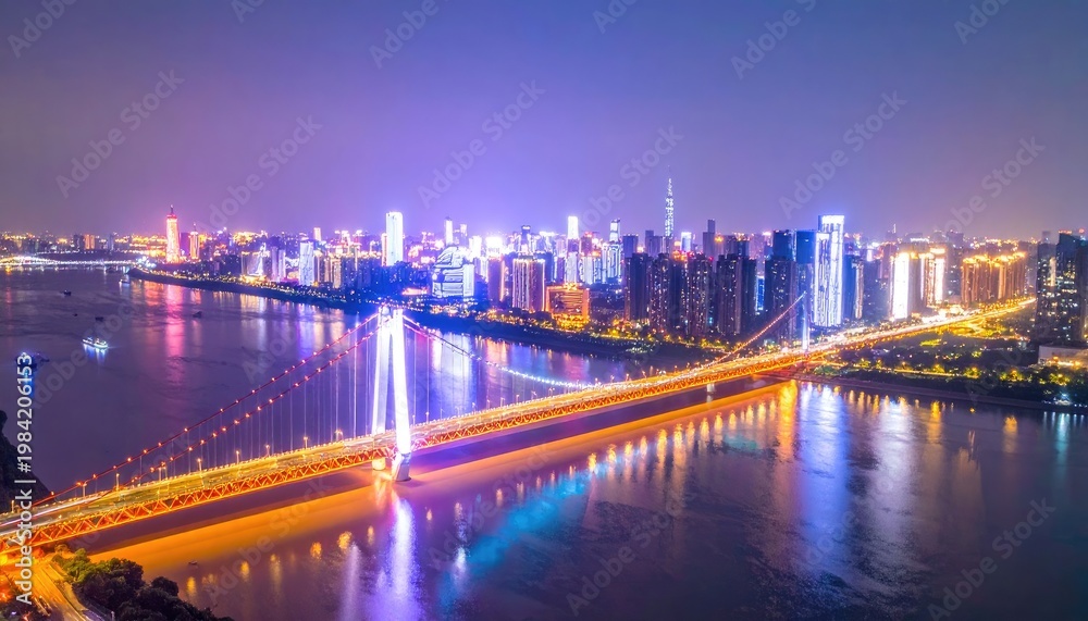 Obraz premium A stunning aerial view showcases a vibrant cityscape illuminated at night, connected by a gracefully arched bridge over a tranquil river.