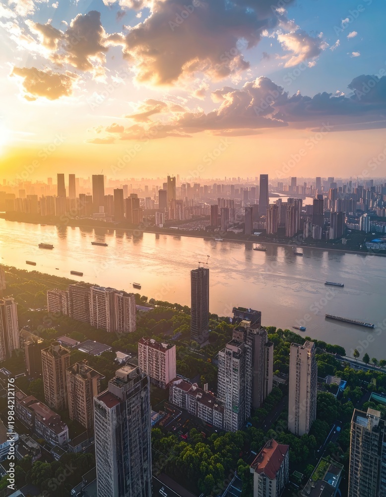 Fototapeta premium An aerial view showcases a sprawling cityscape along a wide river at sunset, bathed in warm golden light and framed by dramatic clouds.