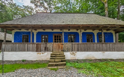 Photos Traditional Romanian peasant house with a blue exterior and a shingled roof, featuring a wooden porch and stone steps