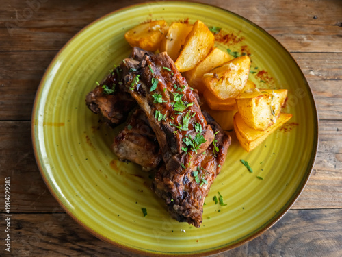 BBQ pork ribs with a sweet and tangy glaze, served with a side of crispy roasted potato wedges, garnished with fresh parsley on a lime green plate.