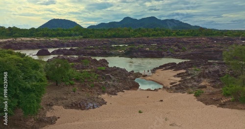 A scenic aerial view of a winding river flowing through rugged rocky terrain, surrounded by lush green forest and sandy riverbanks. The natural composition highlights untouched wilderness beauty.