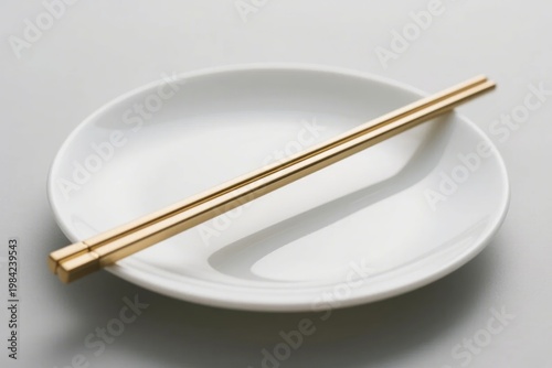 A pair of golden chopsticks resting on a white ceramic plate against a neutral background