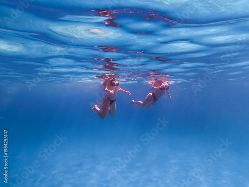 Two women swimming underwater in the crystal clear turquoise water of the Red Sea in Egypt during summer vacation