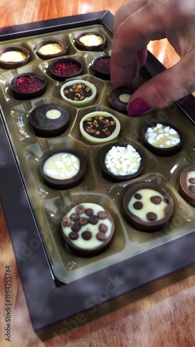 Vertical video social media - Closeup of newly opened box of chocolates and a woman’s hand taking one to eat from the variety of colors, shapes and textures.