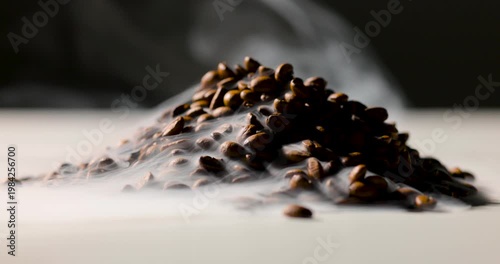 A pile of roasted coffee beans emits gentle steam, creating a rich, aromatic atmosphere against a dark background. Shallow depth of field highlights texture and warmth