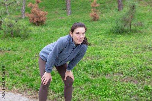 Wallpaper Mural Athletic woman in gray fleece and brown leggings is taking a break while jogging outdoors, showing determination and focus in a lush green park environment Torontodigital.ca
