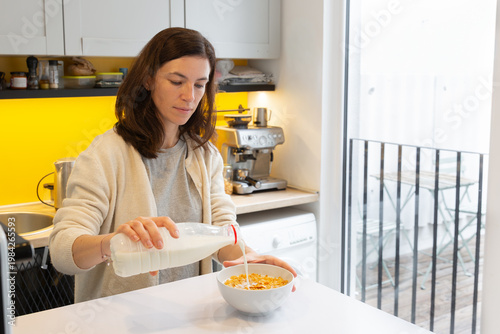 Wallpaper Mural Woman pouring milk into a bowl of cereal while standing in a modern kitchen with bright yellow accents, showcasing a healthy breakfast routine and home environment Torontodigital.ca