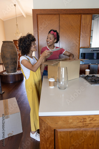 Photos Diverse female friends wearing yellow overall dress and red tee unpacking boxes