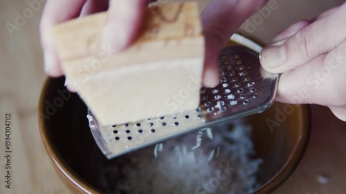 Macro close-up of cheese being grated on metal grater into brown plate. Fresh food preparation, cooking process, kitchen scene, shredded cheese texture.