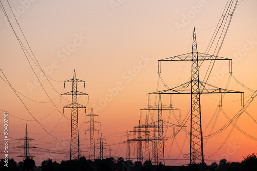 Εκτύπωση καμβά Silhouette of several high-voltage power lines and electricity pylons against a glowing orange and red sunset sky in Germany