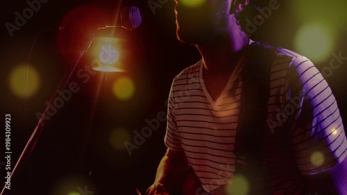 Camera pulling back, musician playing red guitar and singing into mic, performing under amber lamp